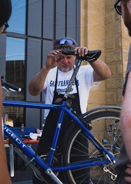 Un homme répare un vélo, deux personnes regarde (photo Sven Becker)