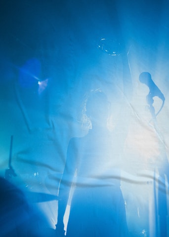 Femme sur scène à contre-jour, lumière bleue, micro à l'avant-plan